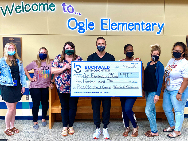 Doctor Buchwald holding 500 dollar check for Ogle Elementary School for winning back to school contest