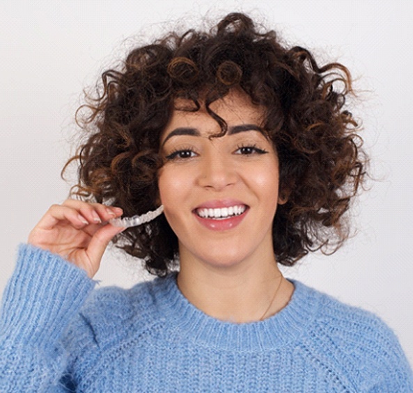 A woman wearing a blue sweater holding an Invisalign aligner and smiling