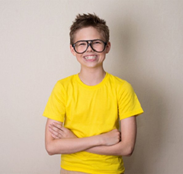 Boy with glasses and yellow shirt smiling proudly showing off his braces