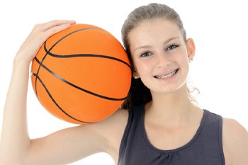 Smiling girl with braces holding a basketball on her shoulder 