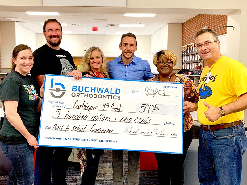 Buchwald Orthodontics team holding check made out to Curtsinger fourth grade classroom for back to school fundraiser