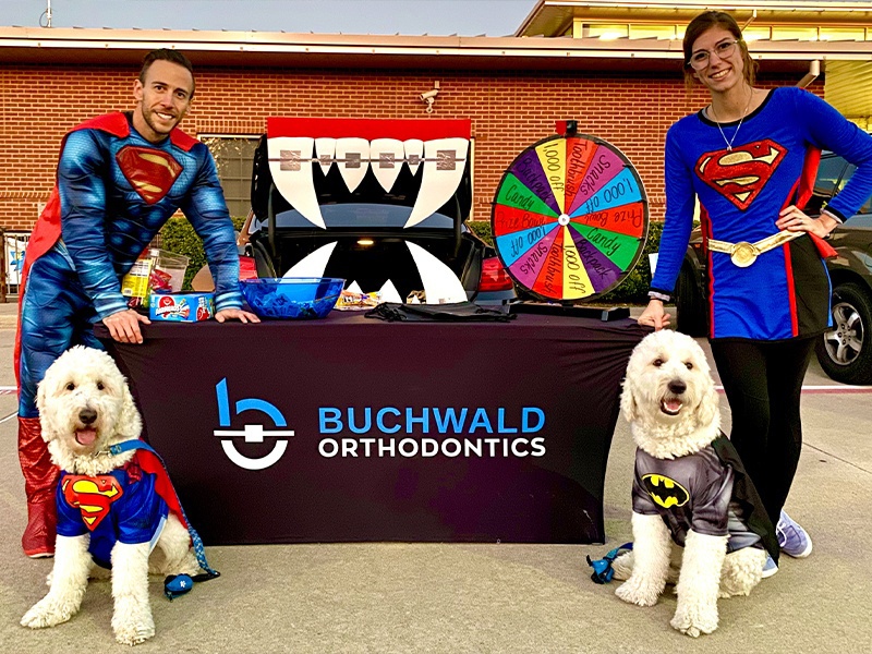 Doctor Buchwald and team member dressed as Superman standing at event table with two dogs