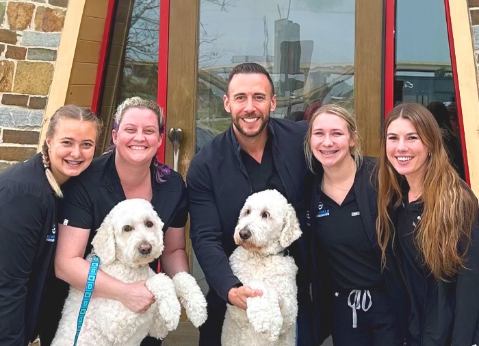 Smiling Frisco and Prosper orthodontic team members smiling with two fluffy white dogs