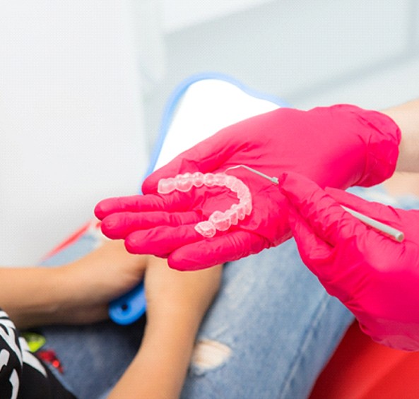 A dental professional with a clear aligner in their hand showing a patient